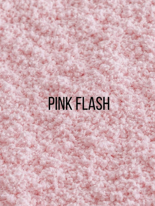 A close-up texture shot of a fluffy pink faux fur or sherpa fabric, with the text 'PINK FLASH' printed in black in the center.