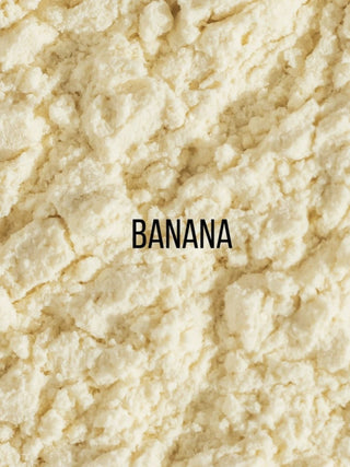 A close-up texture shot of a crumbly, off-white powder, labeled with the word 'BANANA' in black text in the center. The powder resembles banana flour or cocoa powder.