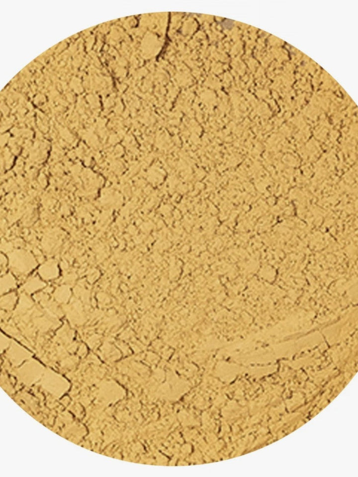 A close-up circular view of a fine, textured golden-yellow powder, likely cosmetic powder or pigment, on a white background.