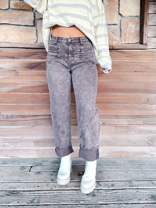 A woman stands against a rustic stone and wood wall wearing a taupe and yellow striped cropped sweater, brown wash jeans, and white platform ankle boots.