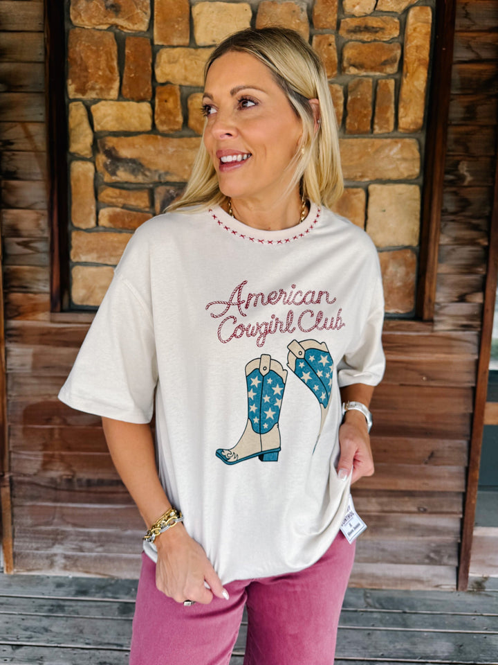 A woman wearing a cream-colored graphic t-shirt with &