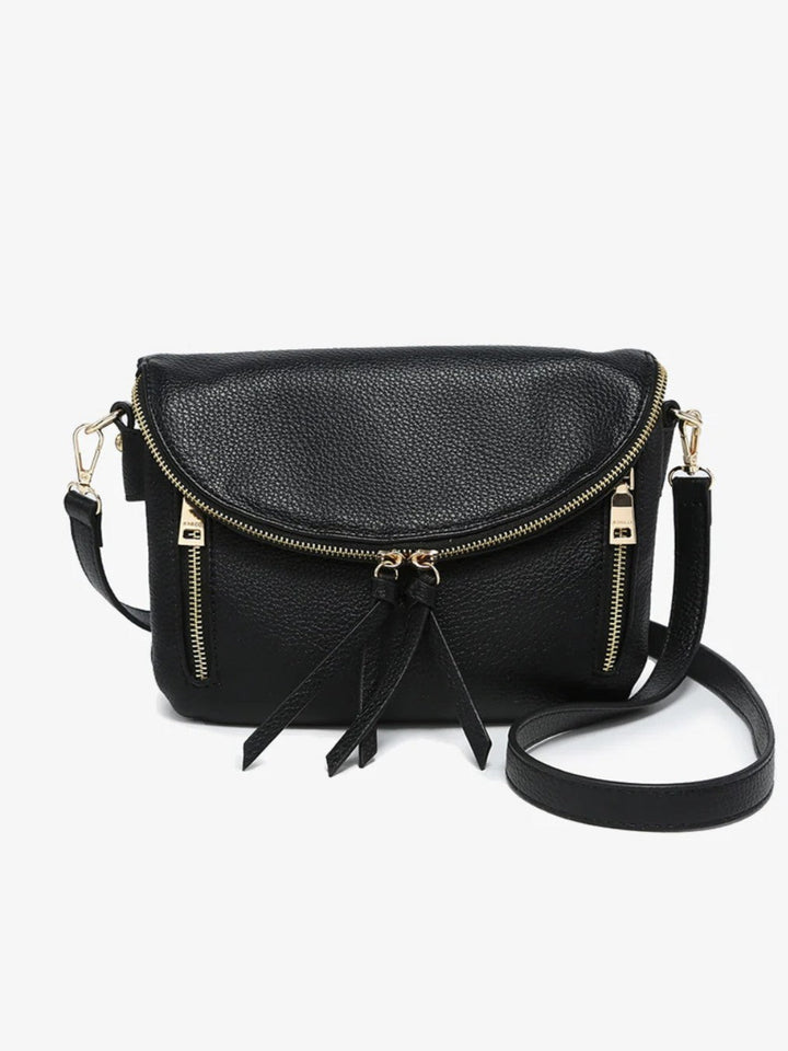 Black pebbled faux-leather crossbody bag with gold-tone hardware, a front zip closure, and a tassel detail, shown on a light gray background.