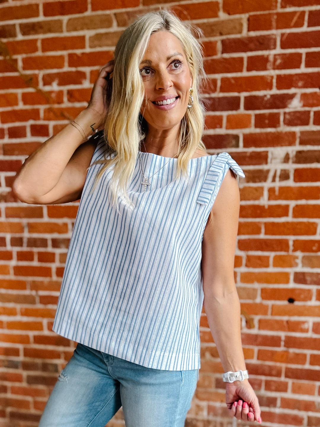 A woman wearing a blue and white vertical striped tank top with shoulder ties and a ruched neckline.