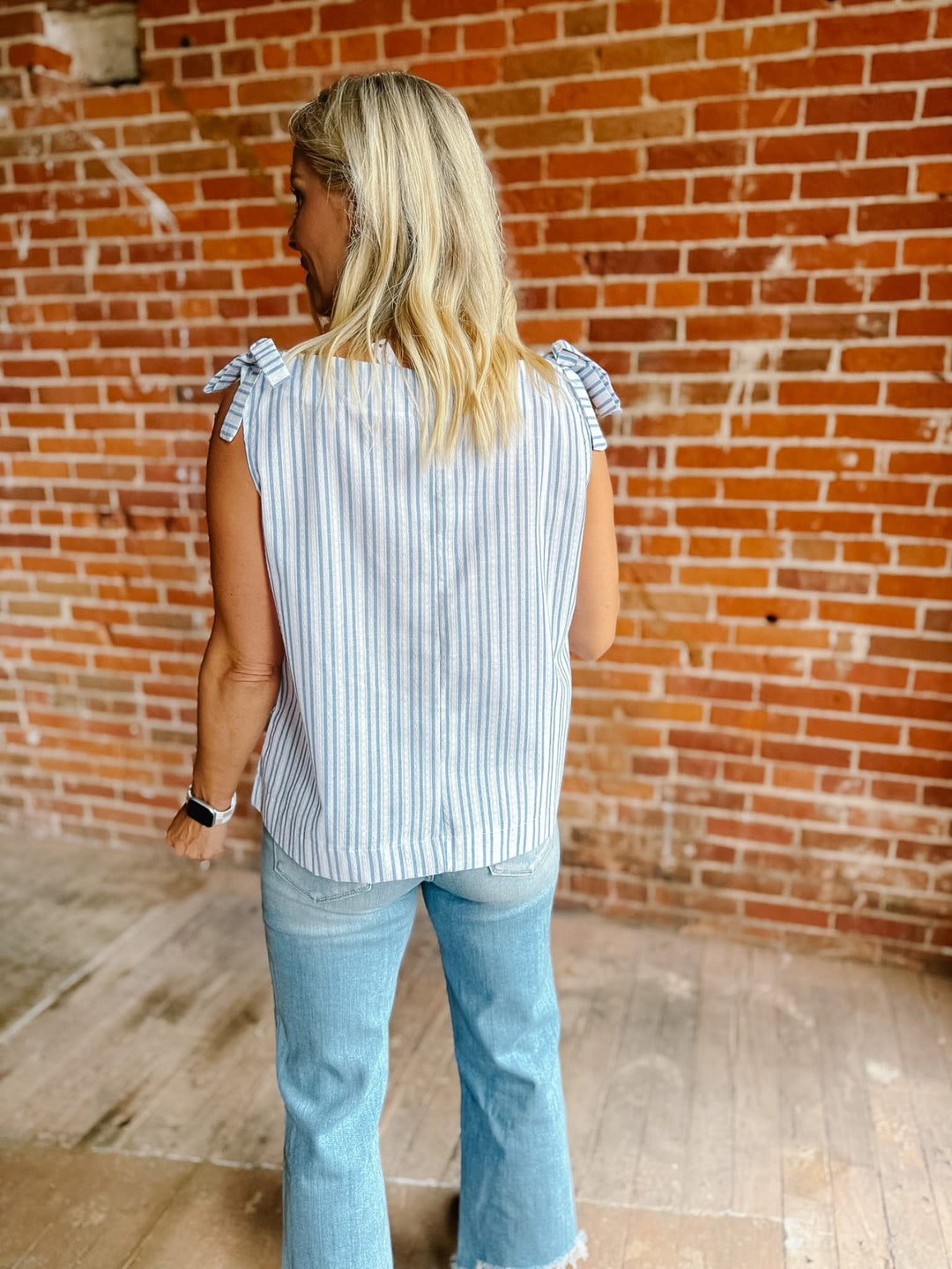 A woman wearing a blue and white vertical striped tank top with shoulder ties and a ruched neckline.
