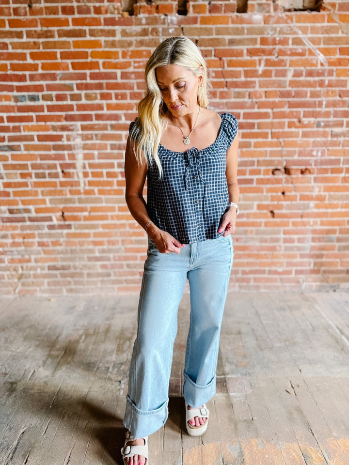 A woman wearing a navy plaid check top with a scoop neckline, button front, and tie detail.