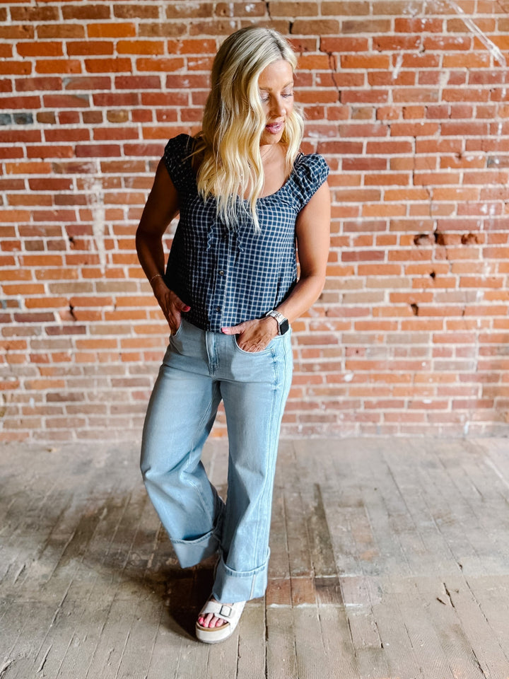 A woman wearing a navy plaid check top with a scoop neckline, button front, and tie detail.