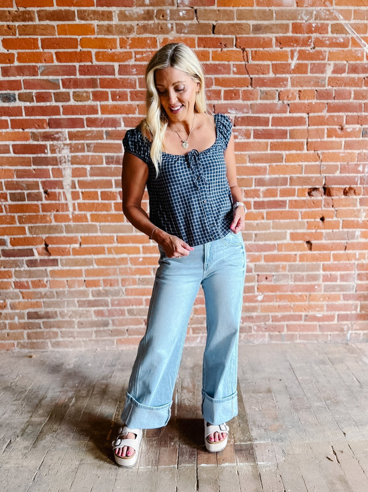 A woman wearing a navy plaid check top with a scoop neckline, button front, and tie detail.