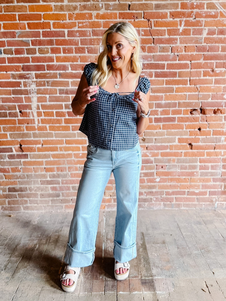 A woman wearing a navy plaid check top with a scoop neckline, button front, and tie detail.