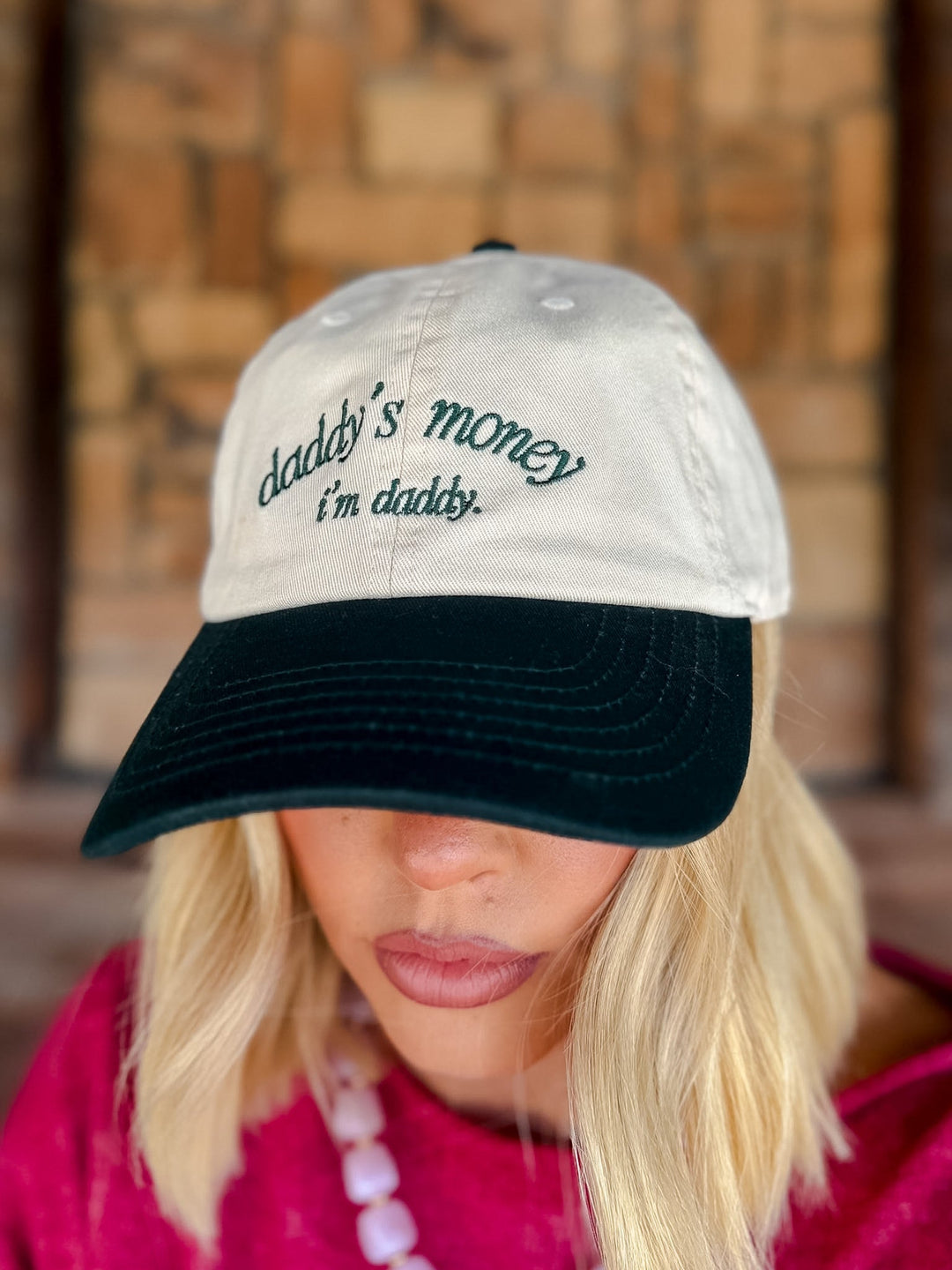 A woman wearing a two-tone baseball cap with a cream crown and a black brim. The cap features the embroidered text &