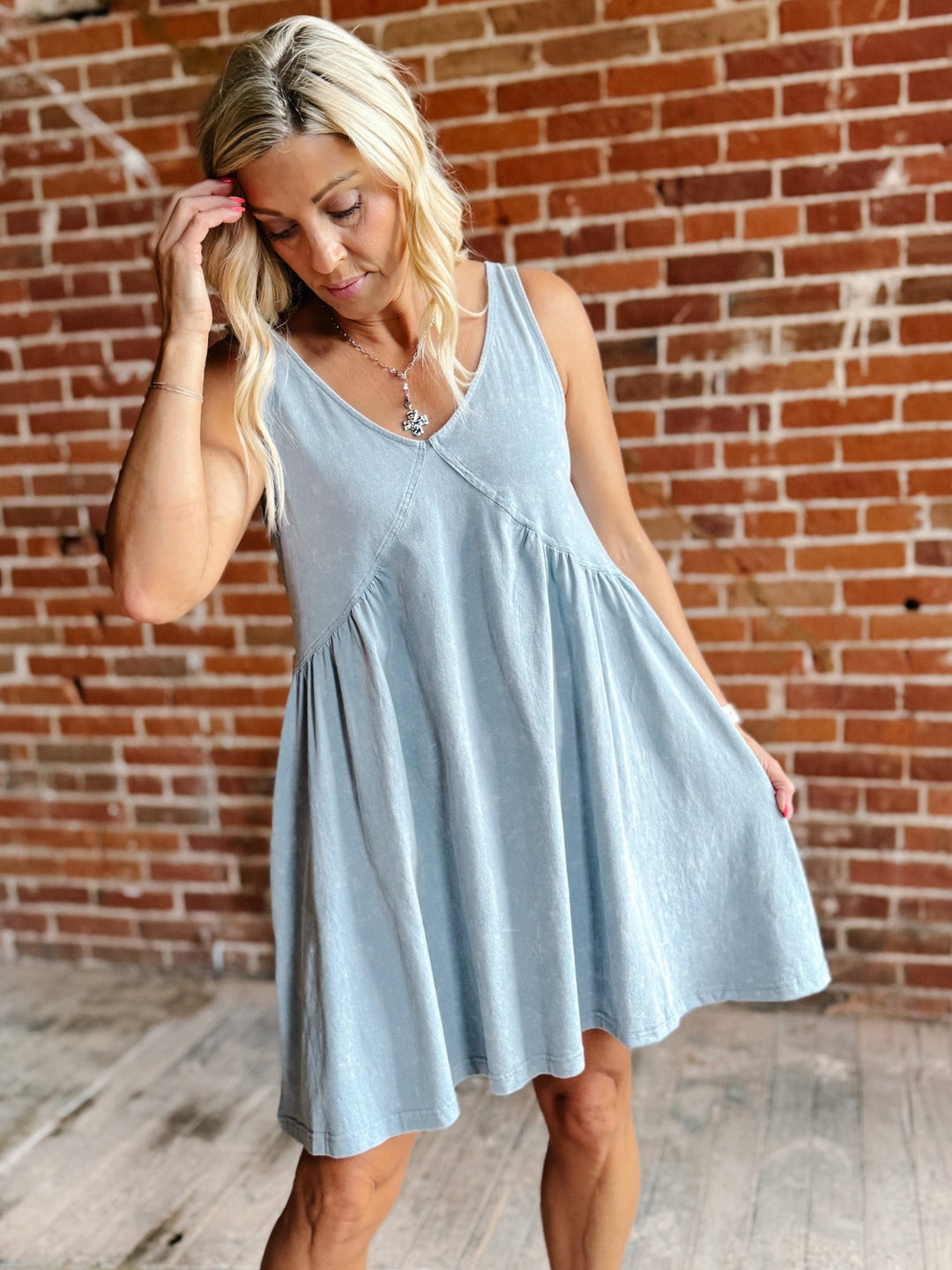 A woman wearing a light blue sleeveless mini dress with a V-neckline and a flowy silhouette, standing against a brick wall.