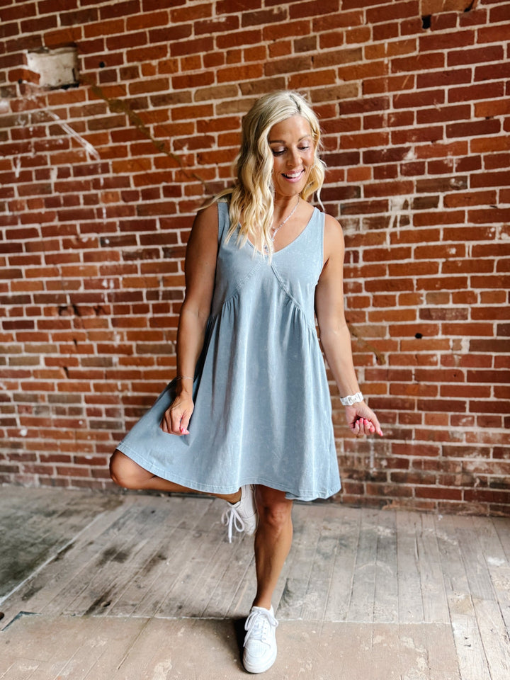 A woman wearing a light blue sleeveless mini dress with a V-neckline and a flowy silhouette, standing against a brick wall.