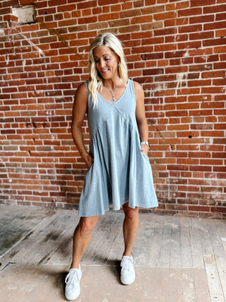 A woman wearing a light blue sleeveless mini dress with a V-neckline and a flowy silhouette, standing against a brick wall.