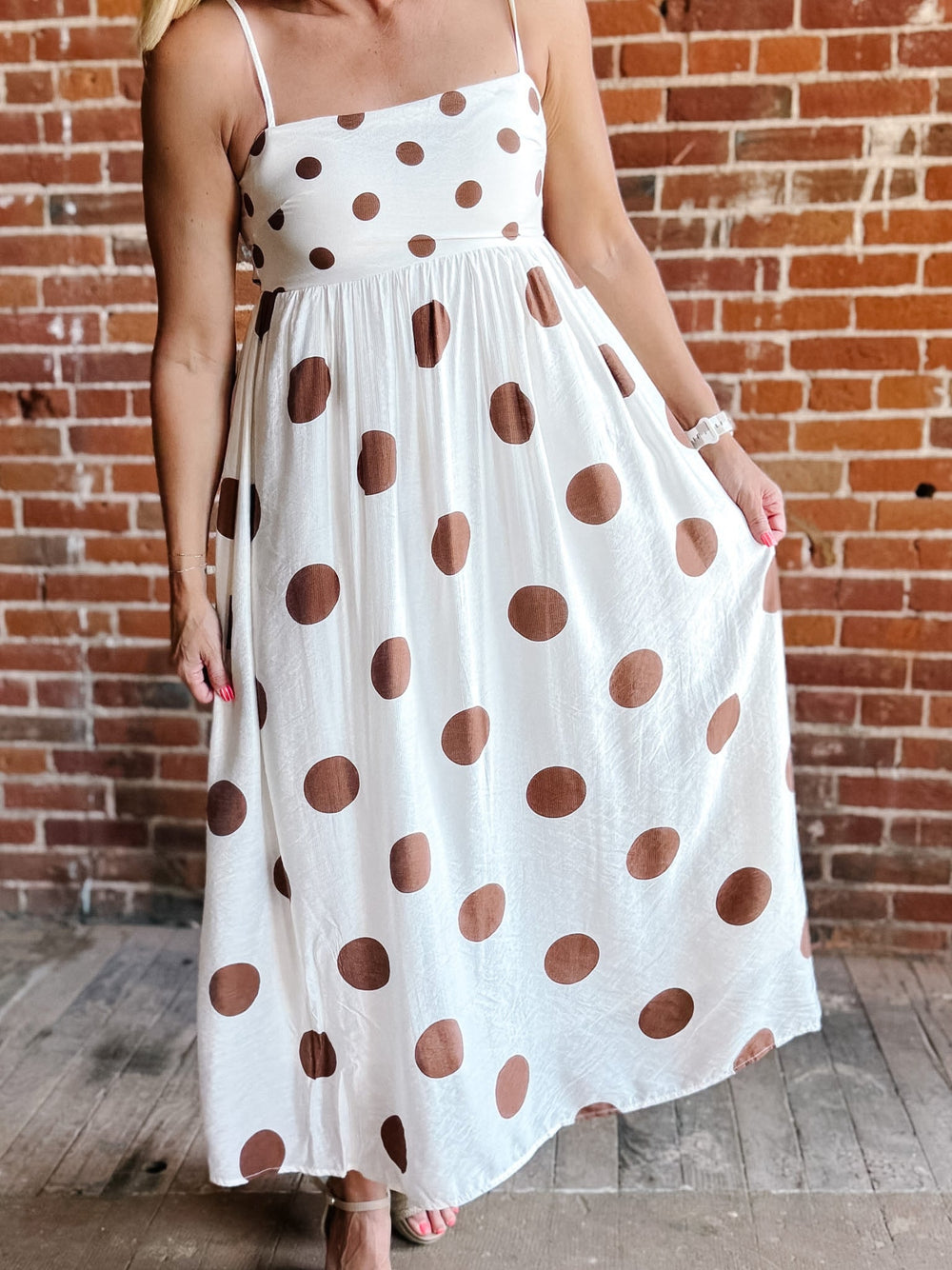 Woman wearing a white midi dress with oversized mocha polka dots, adjustable spaghetti straps, and an empire waist.