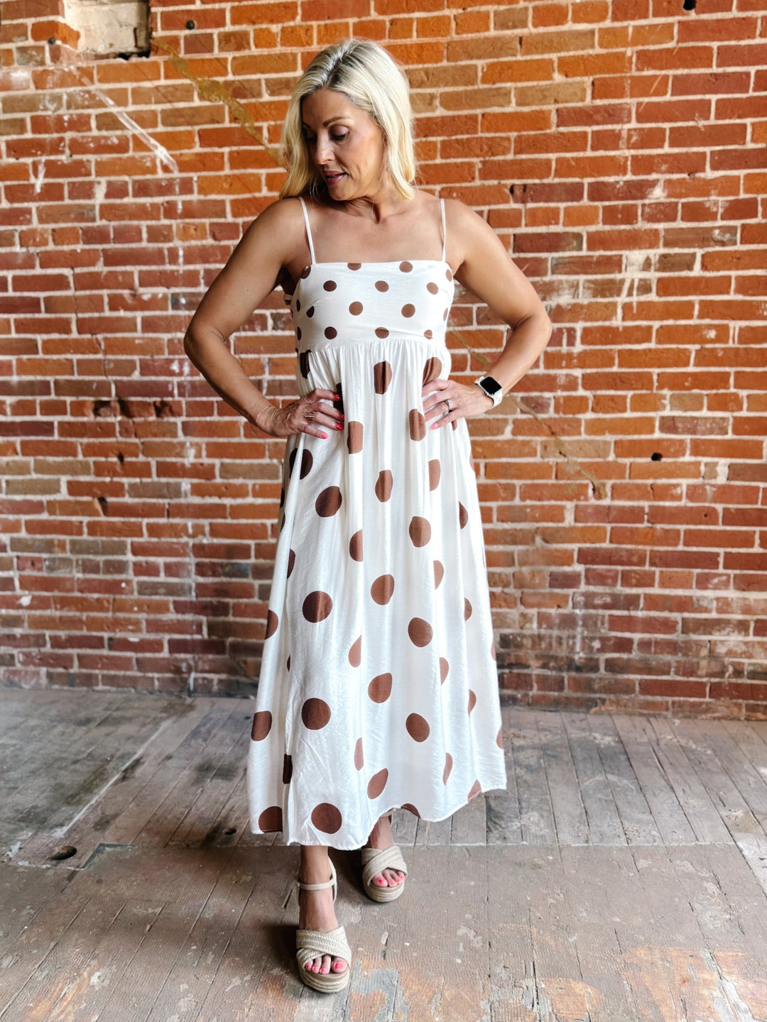 Woman wearing a white midi dress with oversized mocha polka dots, adjustable spaghetti straps, and an empire waist.