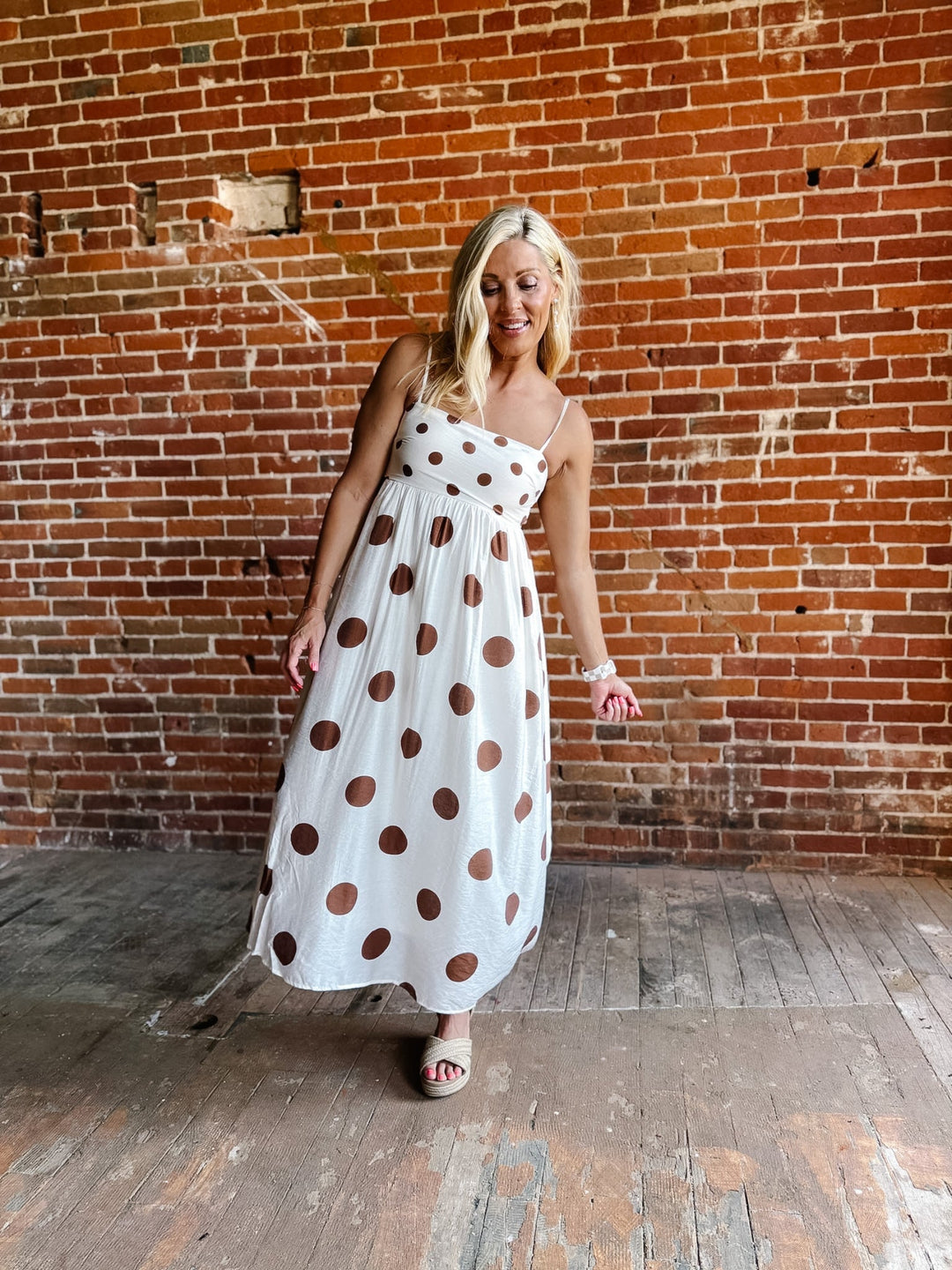 Woman wearing a white midi dress with oversized mocha polka dots, adjustable spaghetti straps, and an empire waist.