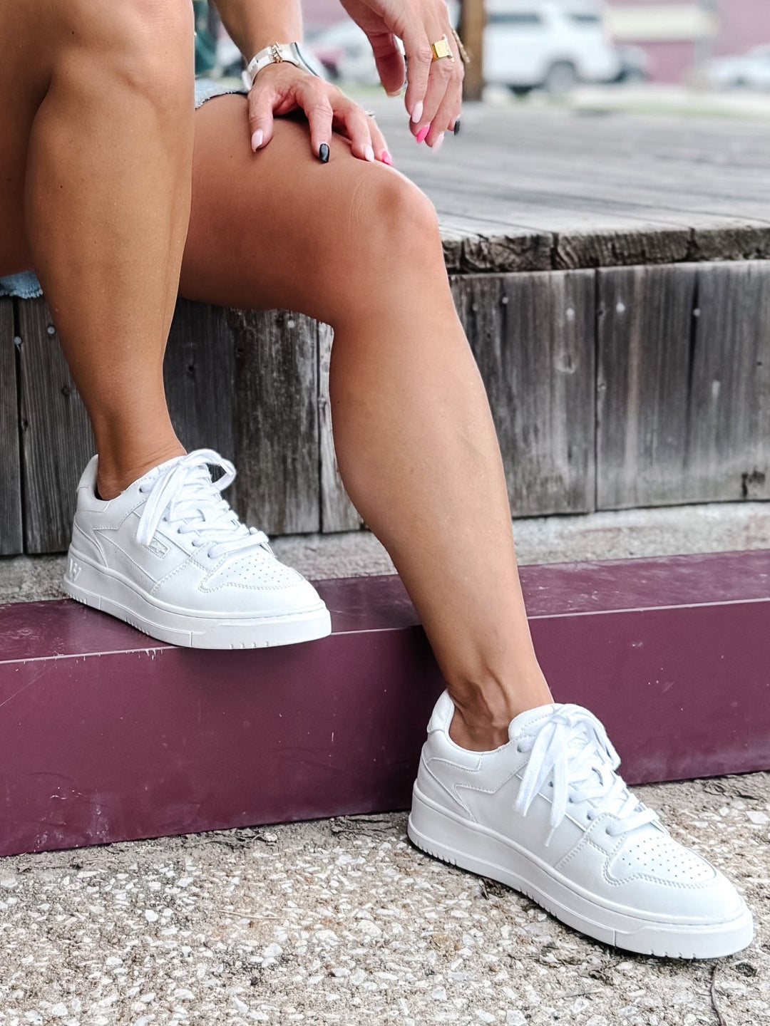 Person wearing white low top sneakers with a lace-up design and perforated toe box detail.