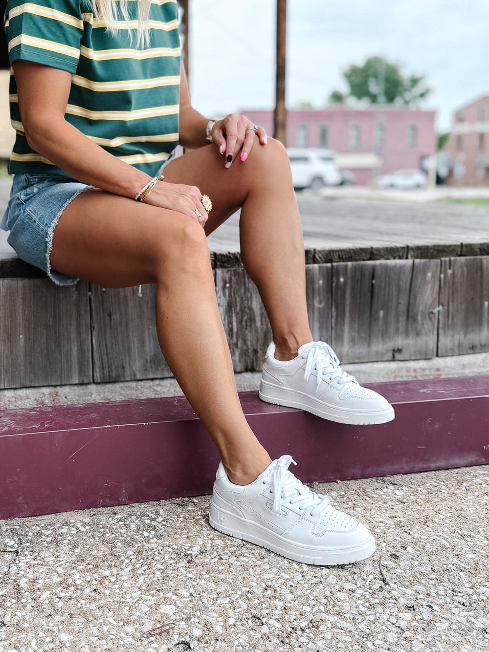 Person wearing white low top sneakers with a lace-up design and perforated toe box detail.