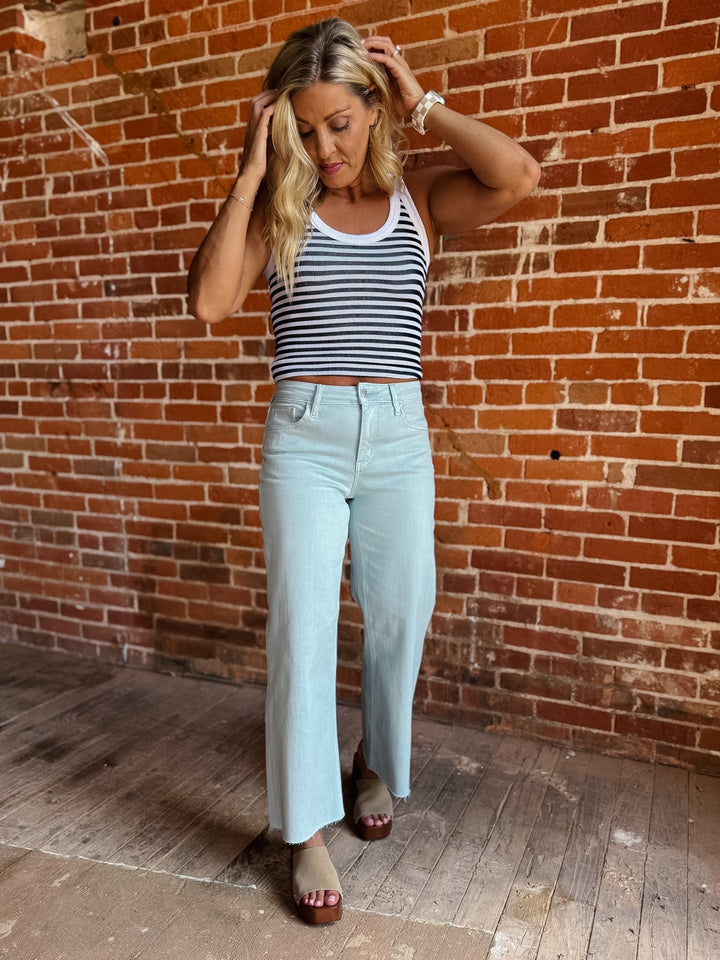 Model wearing wide leg crop jeans in Winter Sky with striped tank and sandals.