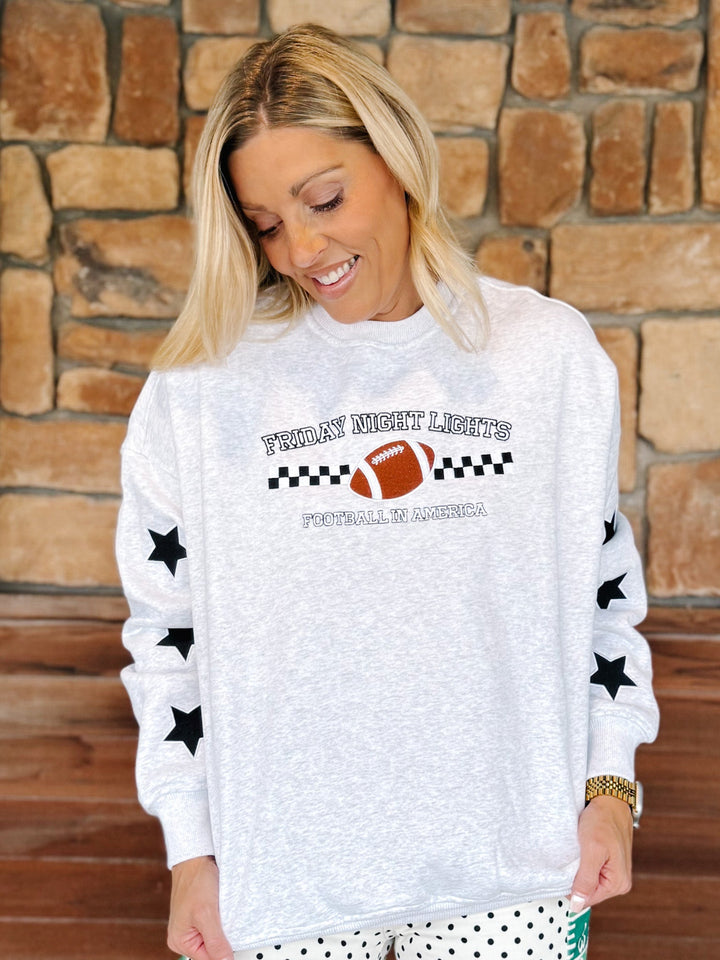 A woman wearing a white heathered long-sleeve sweatshirt with a &