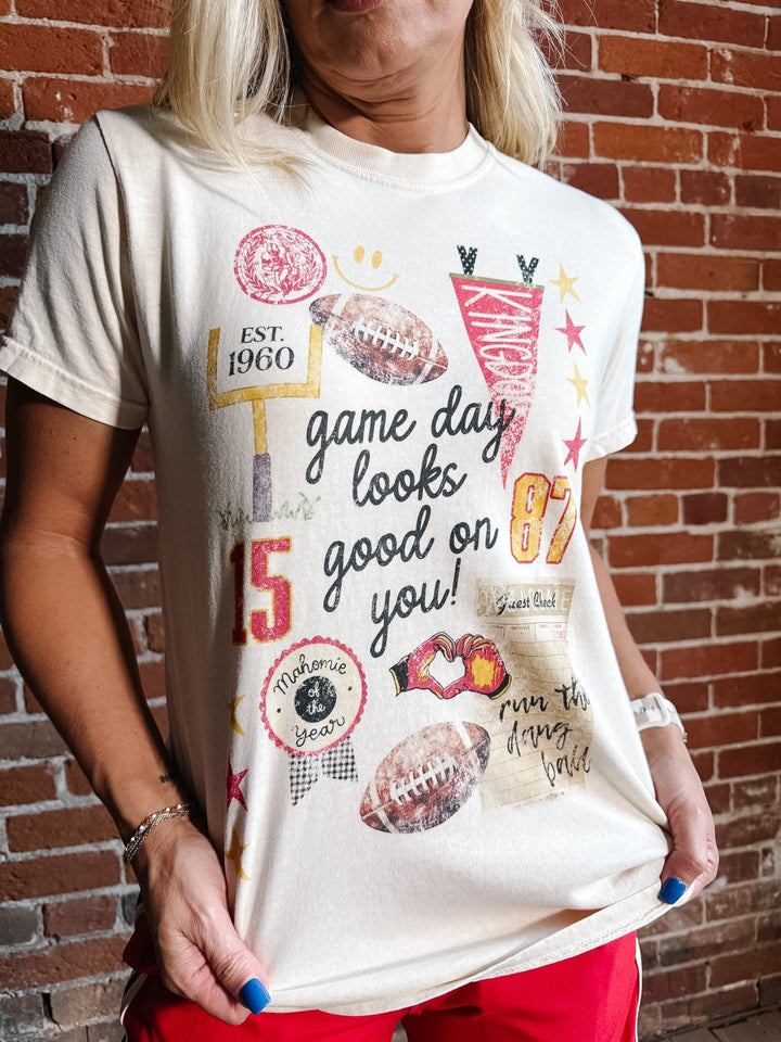 A woman wearing a cream-colored graphic t-shirt with football-themed designs and the text &