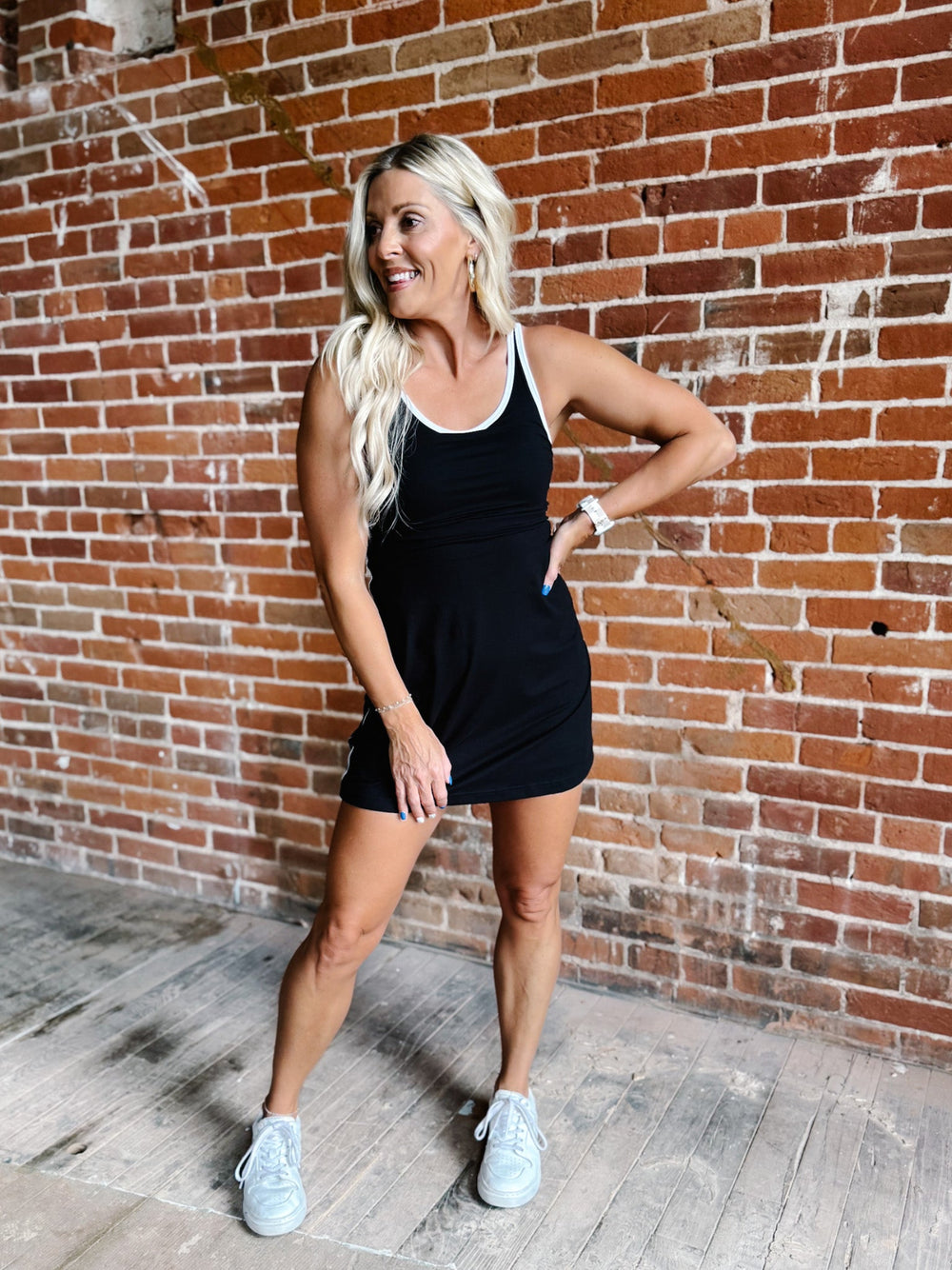 A woman wearing a black skortsie dress with a scoop neckline and contrast trim, stylishly posing indoors.