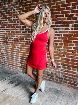 A woman wearing a red skortsie dress with a scoop neckline and contrast trim, stylishly posing indoors.
