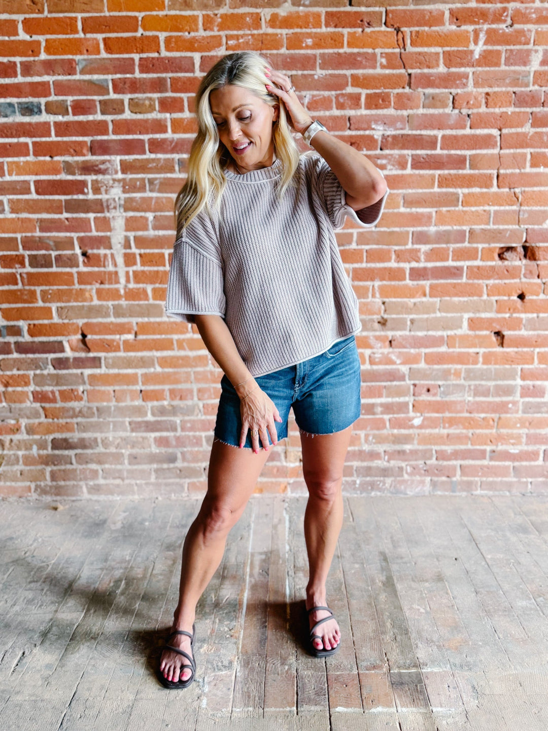 Woman wearing a soft knit sweater with exposed seams and short sleeves, standing against a brick wall.
