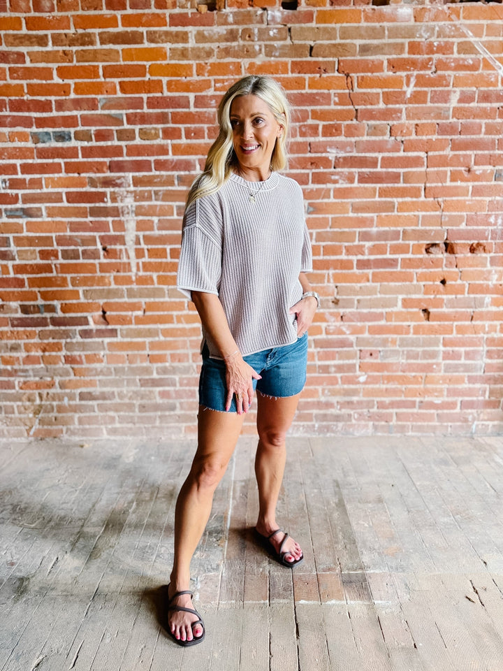 Woman wearing a soft knit sweater with exposed seams and short sleeves, standing against a brick wall.
