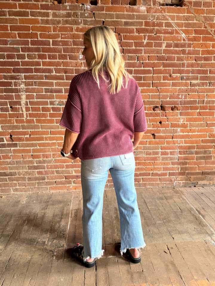 Woman wearing a soft knit sweater with exposed seams and short sleeves, standing against a brick wall.