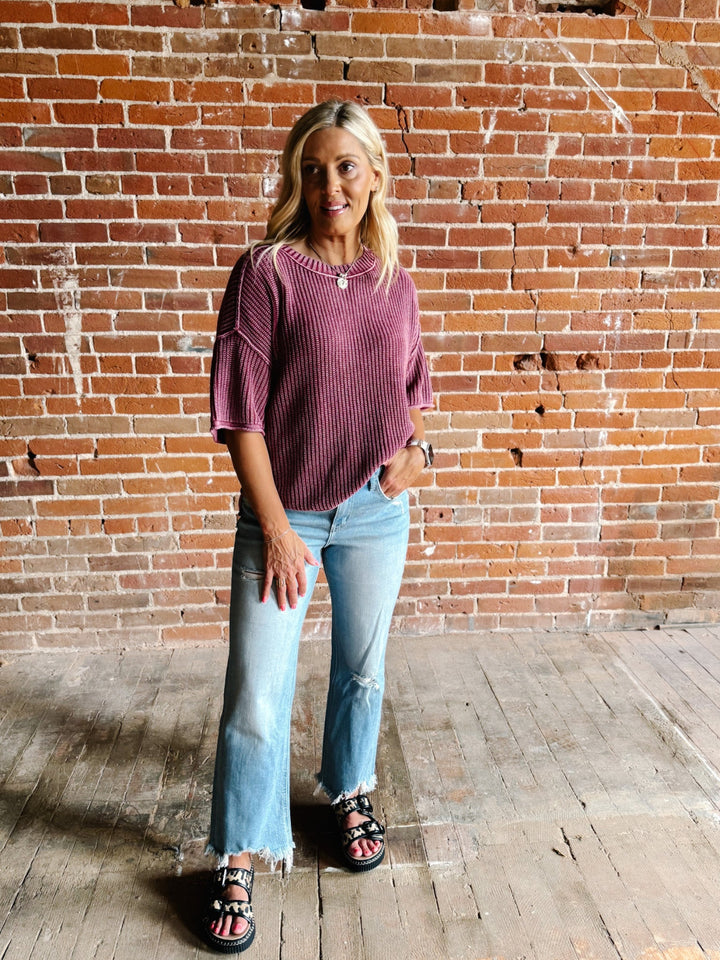 Woman wearing a soft knit sweater with exposed seams and short sleeves, standing against a brick wall.