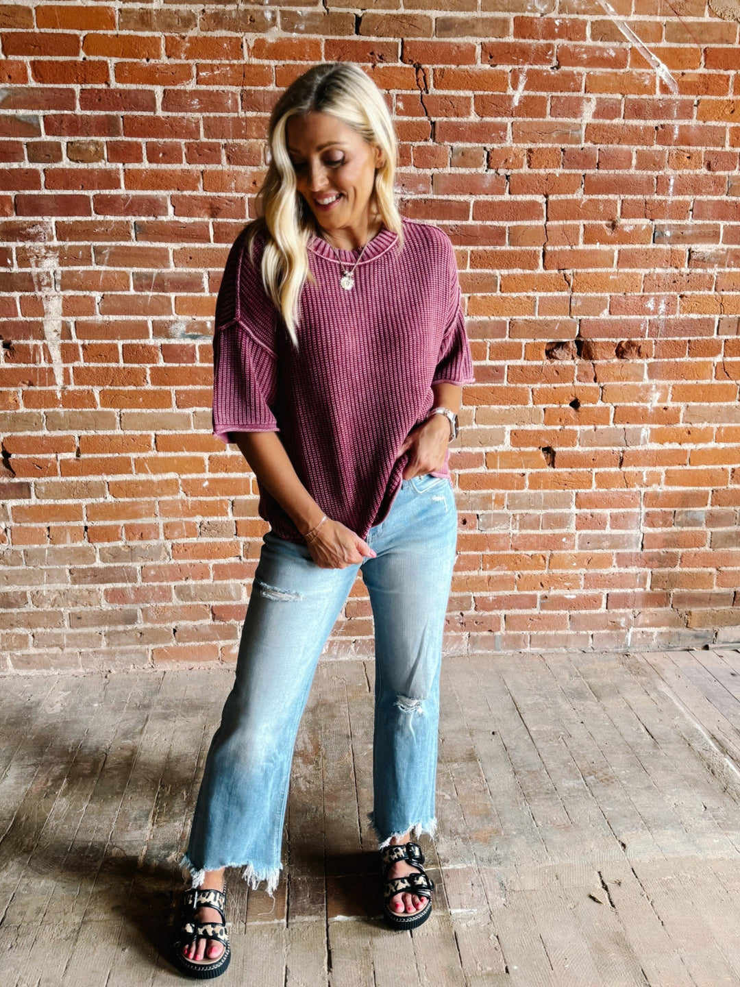 Woman wearing a soft knit sweater with exposed seams and short sleeves, standing against a brick wall.