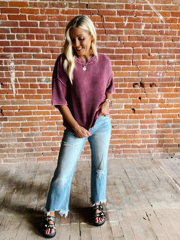 Woman wearing a soft knit sweater with exposed seams and short sleeves, standing against a brick wall.