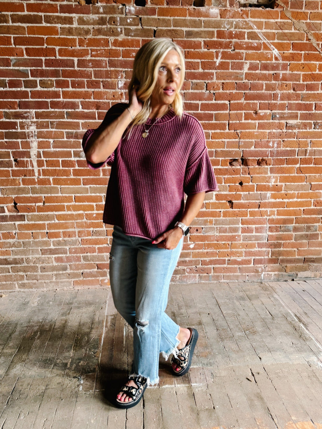Woman wearing a soft knit sweater with exposed seams and short sleeves, standing against a brick wall.