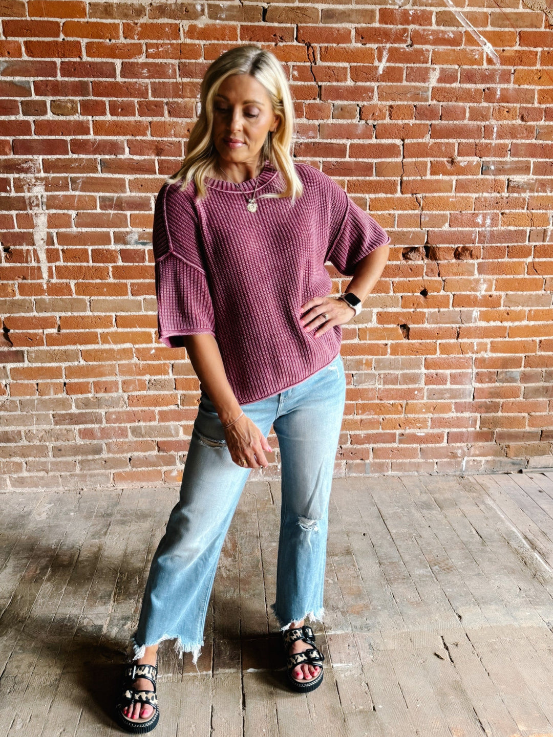 Woman wearing a soft knit sweater with exposed seams and short sleeves, standing against a brick wall.