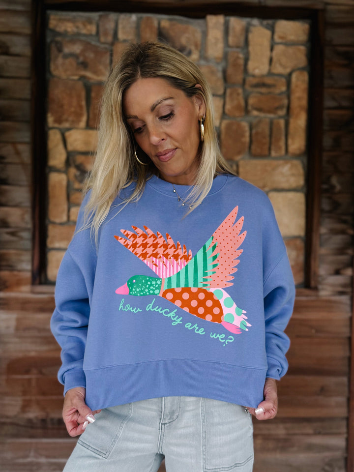 A woman wearing a blue crewneck sweatshirt with a colorful patchwork bird graphic and the text &