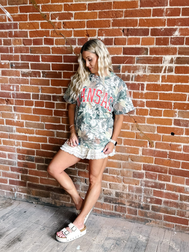 A woman posing against a red brick wall wearing a camouflage graphic t-shirt with &