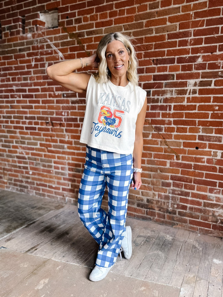 A woman posing in front of a red brick wall wearing a cream sleeveless crop top with a &