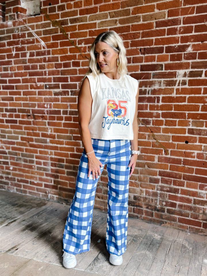 A woman stands in front of a red brick wall wearing a cream sleeveless crop top with a colorful &