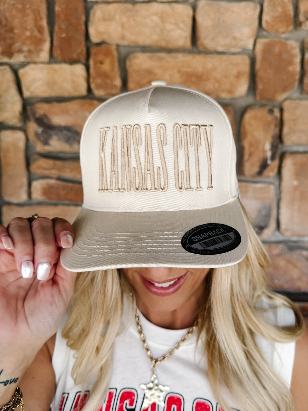 A woman wearing a cream-colored snapback cap with &