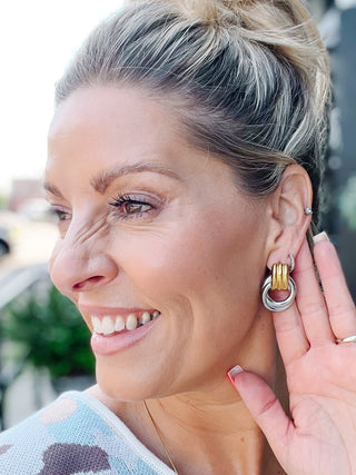 Close-up of sculptural gold and silver two-tone dangle earrings worn by a person.