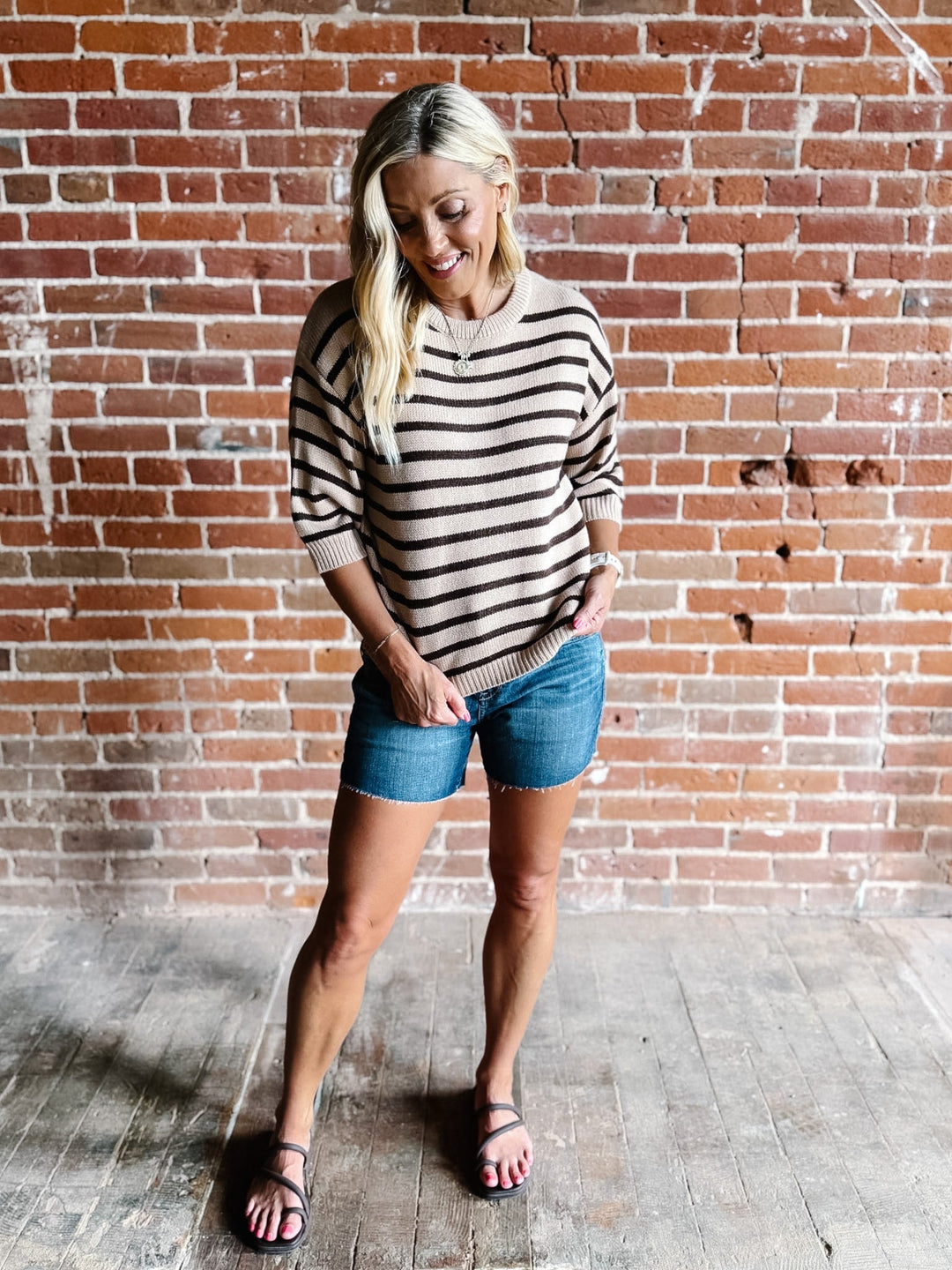 A woman wearing a short sleeve sweater top with mocha stripes and a crew neckline, paired with denim shorts.