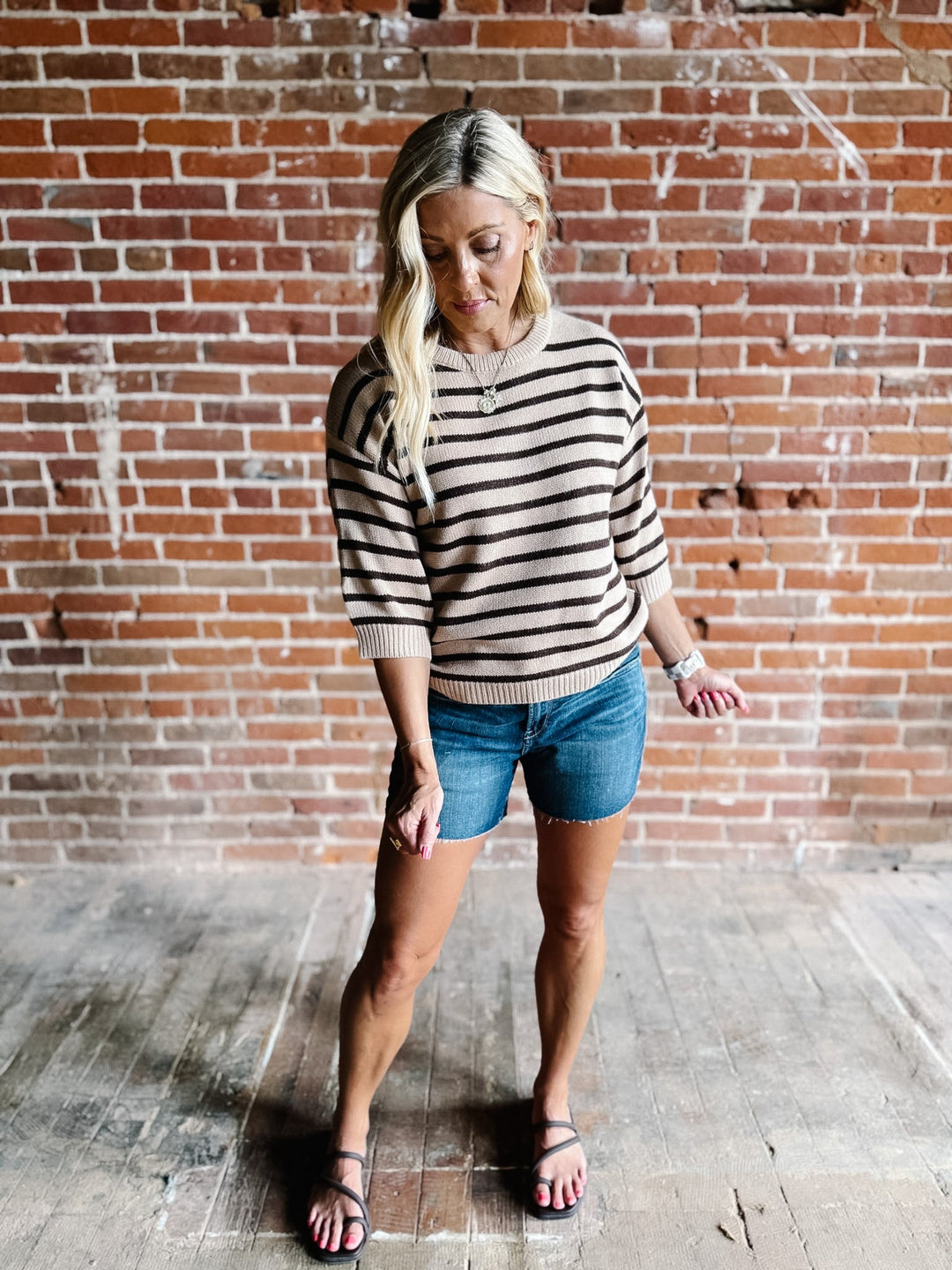 A woman wearing a short sleeve sweater top with mocha stripes and a crew neckline, paired with denim shorts.