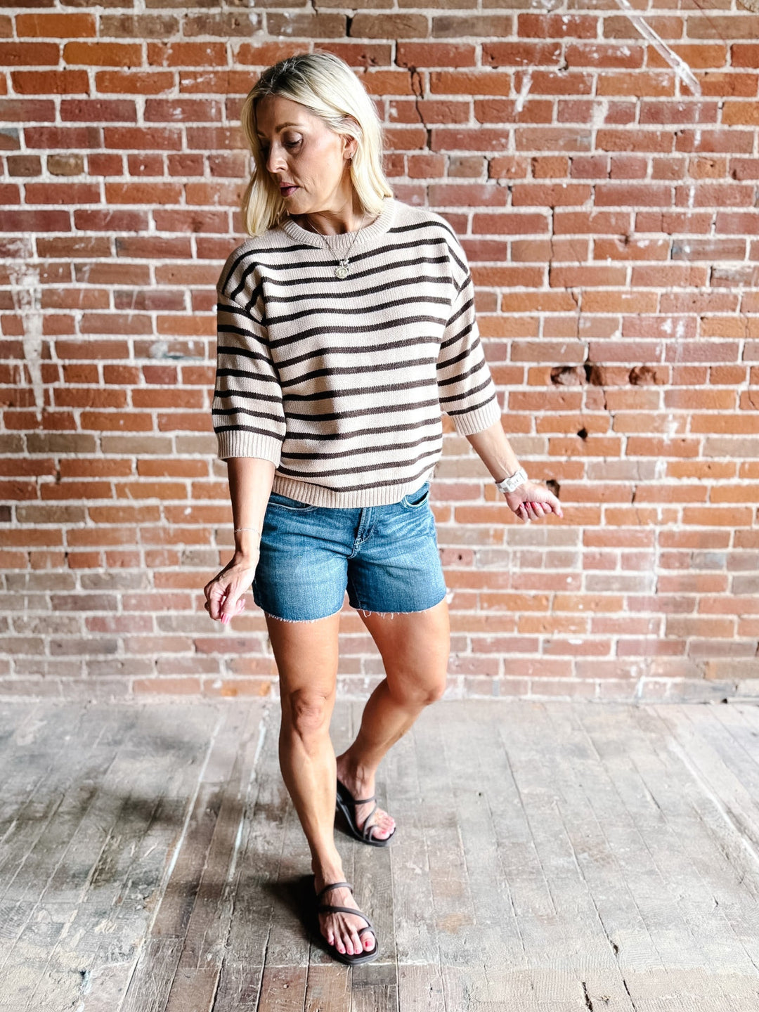 A woman wearing a short sleeve sweater top with mocha stripes and a crew neckline, paired with denim shorts.