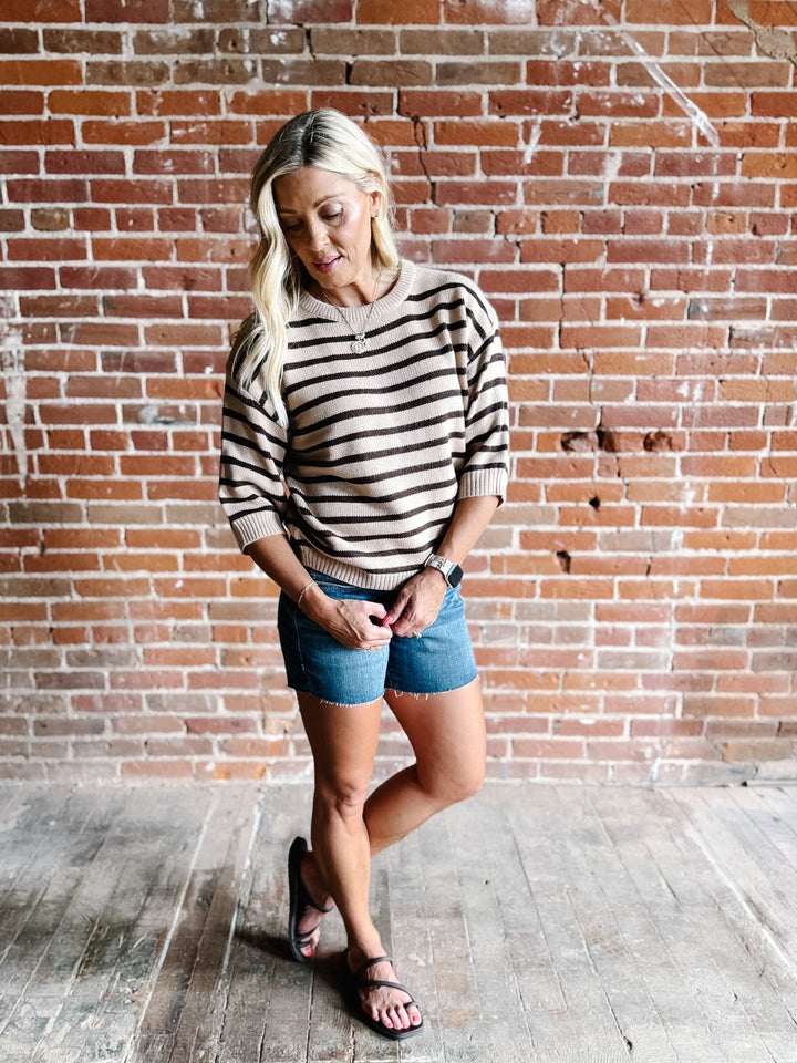 A woman wearing a short sleeve sweater top with mocha stripes and a crew neckline, paired with denim shorts.