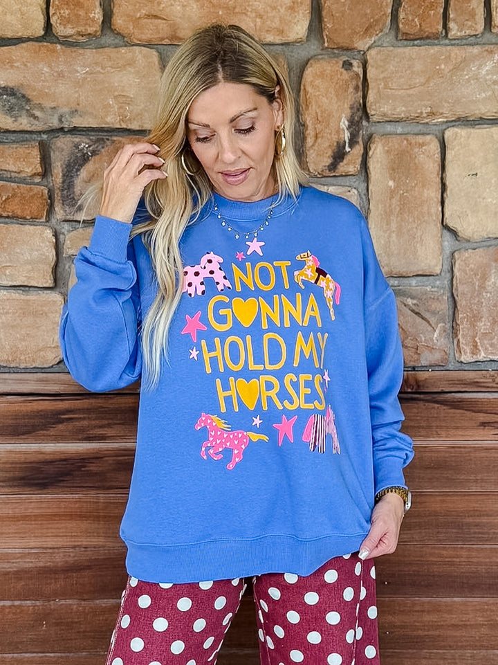 A woman wearing a bright blue crewneck sweatshirt with a colorful graphic that reads &