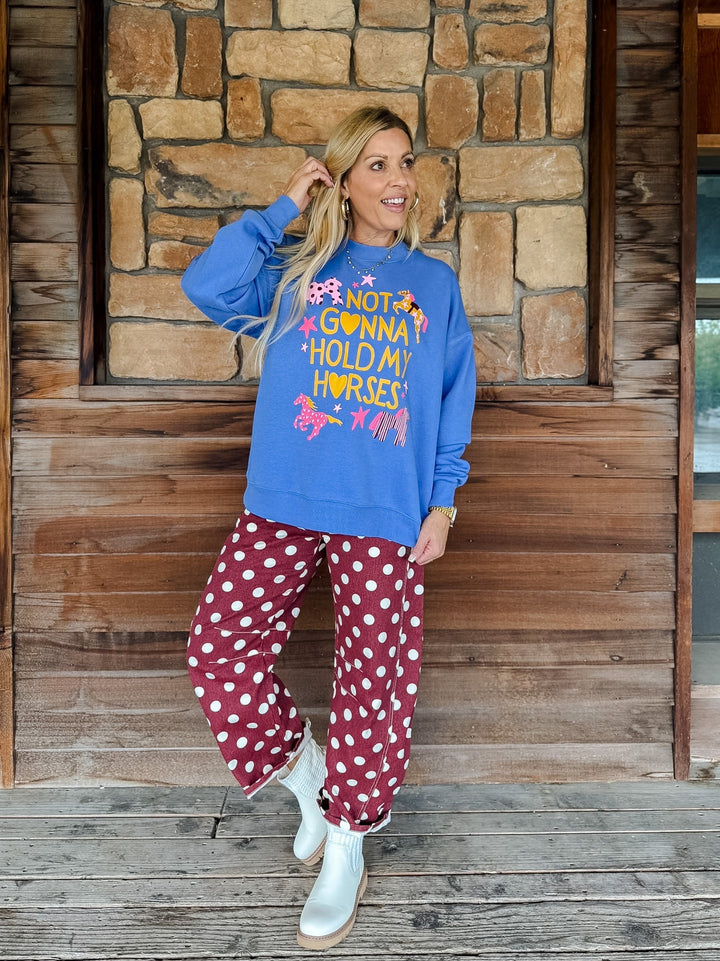A woman posing on a rustic wooden porch wearing a bright blue sweatshirt with a colorful graphic that reads &