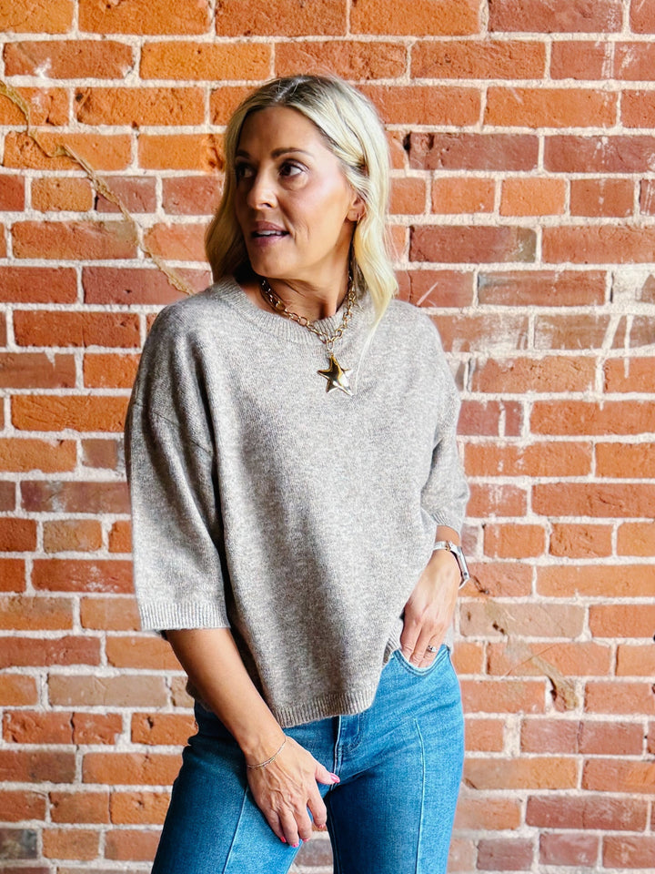 Woman wearing an oatmeal heathered half sleeve sweater with a relaxed fit and crew neckline.