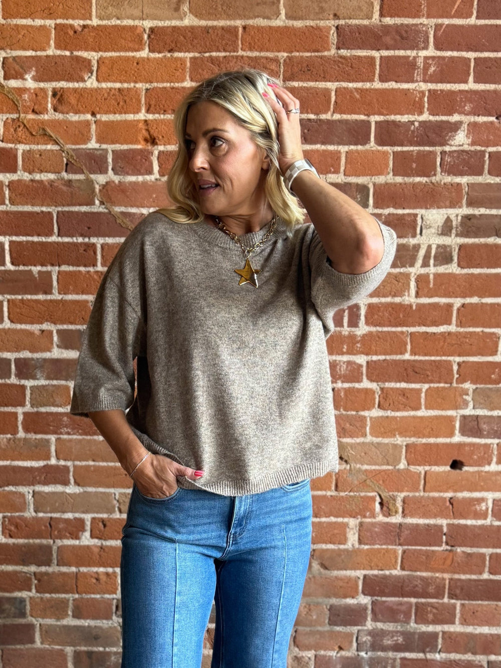 Woman wearing an oatmeal heathered half sleeve sweater with a relaxed fit and crew neckline.