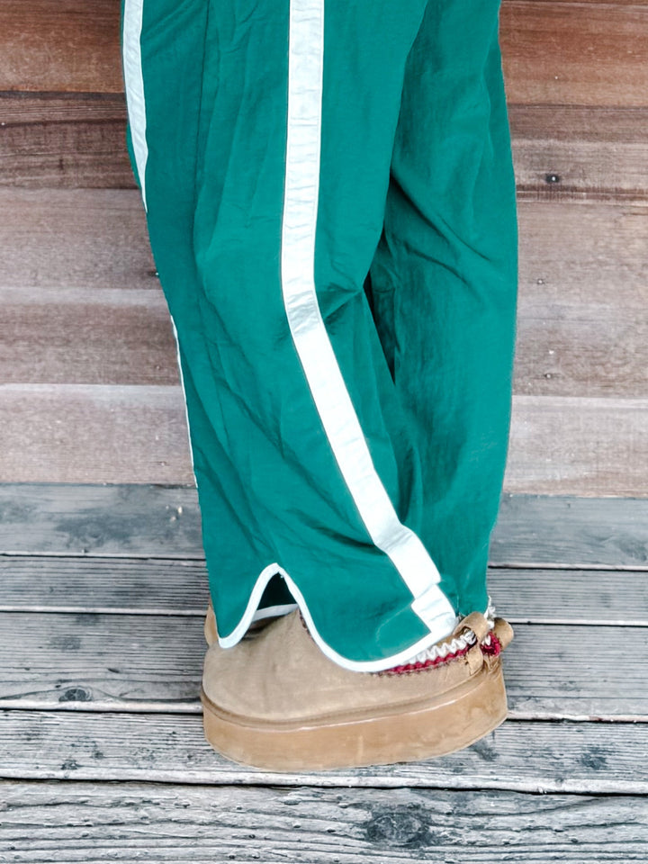 Green wide-leg track pants with a white side stripe, shown on a person&