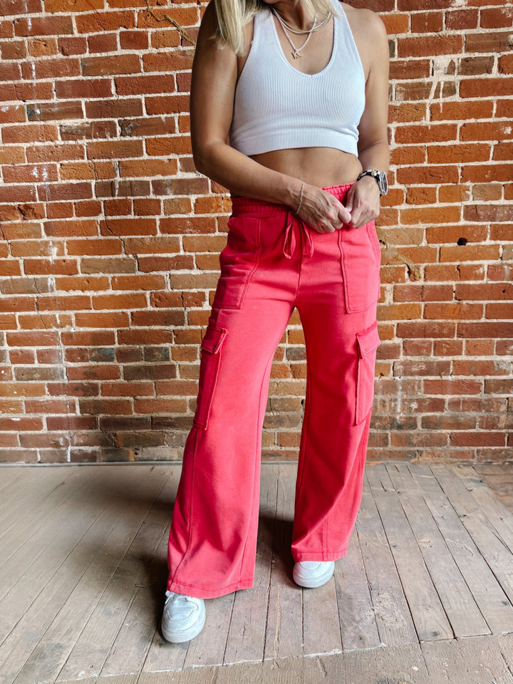 Person wearing bright pink cargo pants and a white top against a brick wall.